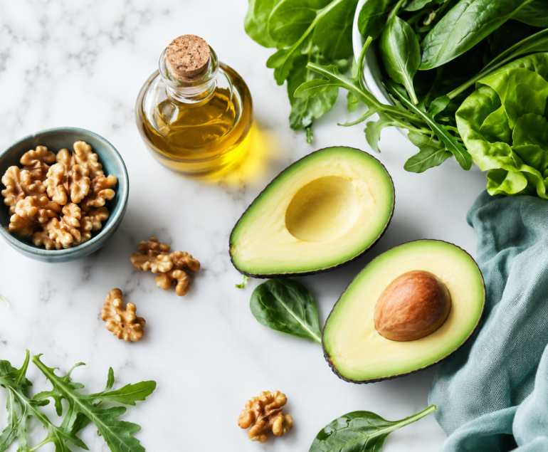Aguacate, nueces y aceite de oliva sobre superficie blanca representando los alimentos típicos de una dieta cetogénica